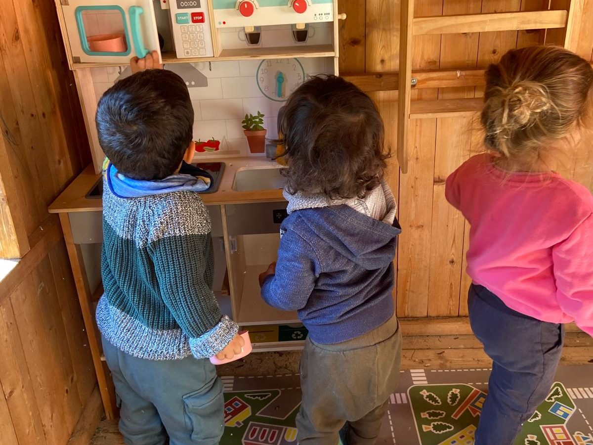 Tres niños de espaldas jugando en una cocinita de madera