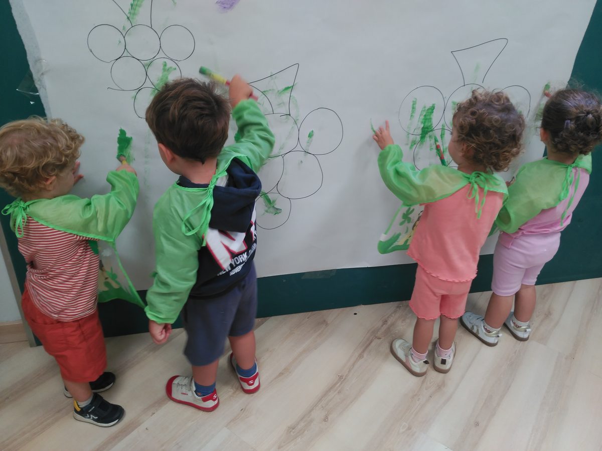 Niños de espaldas pintando racimos de uvas en un mural