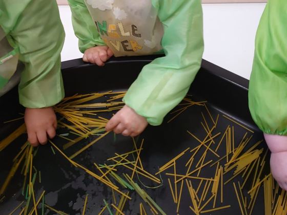 Manos de niños explorando espaguetis crudos en una bandeja negra