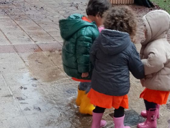 Niños de espaldas con botas de agua pisando charcos