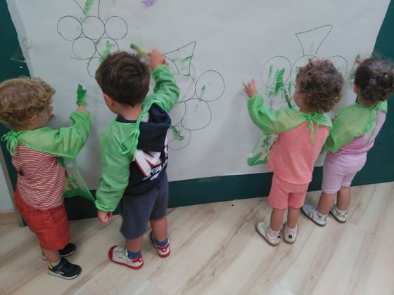Niños de espaldas pintando racimos de uvas en un mural