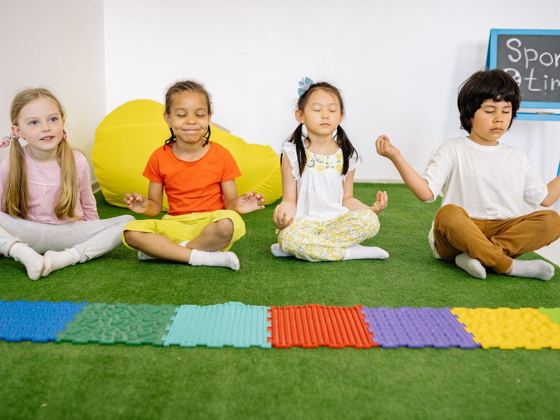 Niños sentados en postura de yoga sobre una alfombra verde