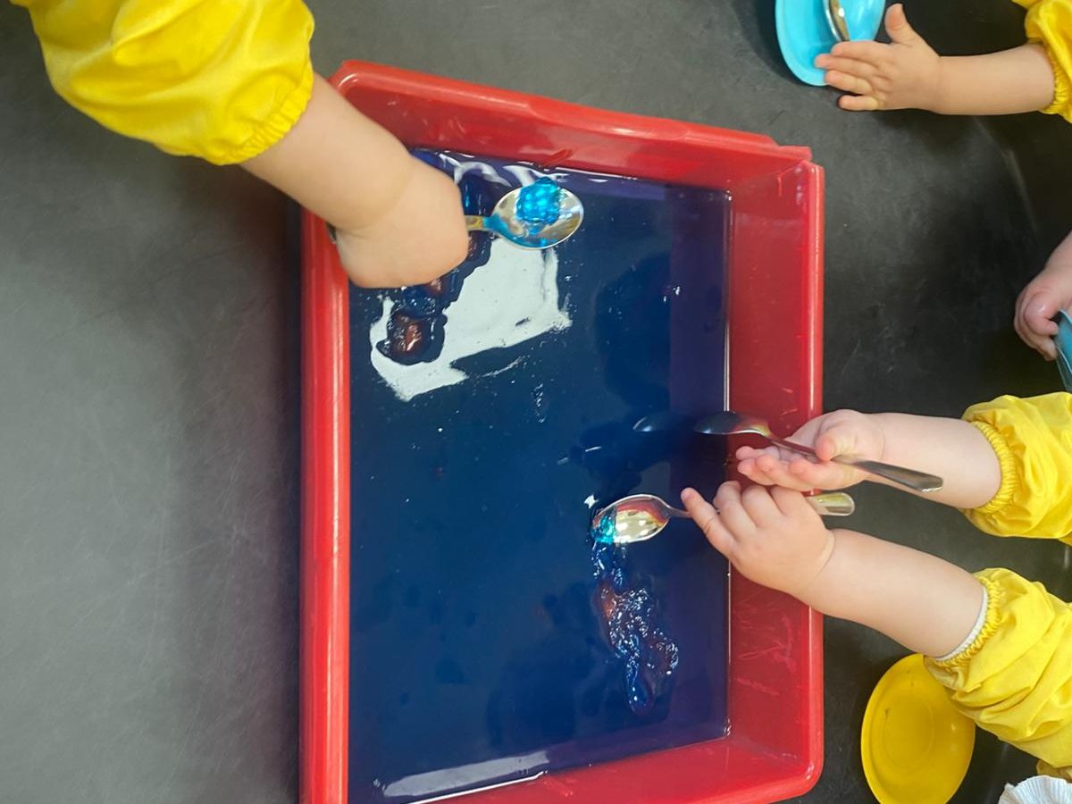 Manos jugando con agua y esponjas en una bandeja roja