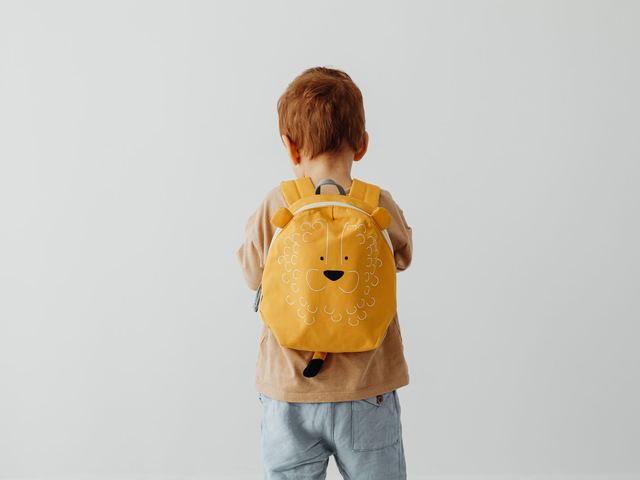 Mochila infantil pequeña junto a unas zapatillas de bebé y una muda de ropa doblada