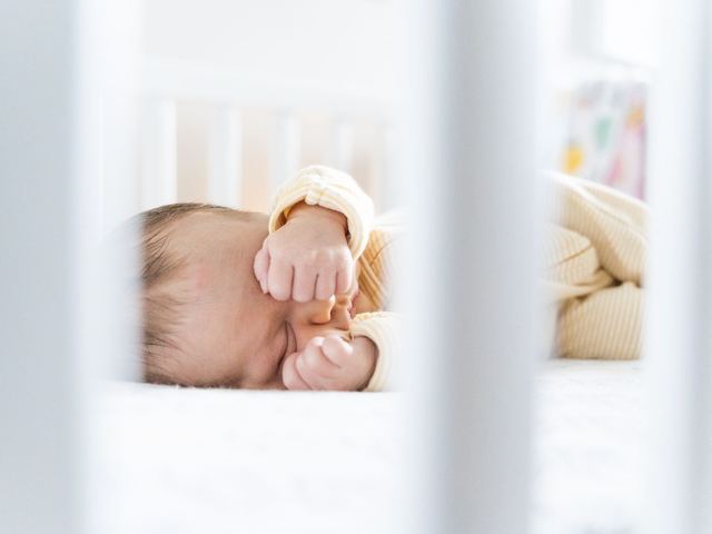 Cuna de madera junto a la cama de los padres, con sábana ajustada y sin cojines ni peluches